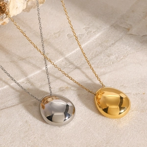 Minimalist round pebble pendant necklace in gold and silver finish on stone background