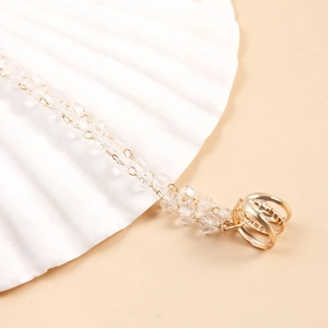 Collier doré ethnique avec perles de cristal facettées et anneaux sur plateau coquillage