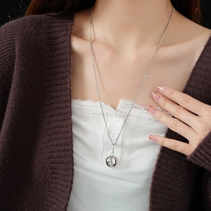 Close-up of a silver spherical pendant on a delicate titanium steel chain necklace
