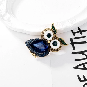 Close-up of owl brooch featuring a large blue pear-cut crystal and rhinestone wings
