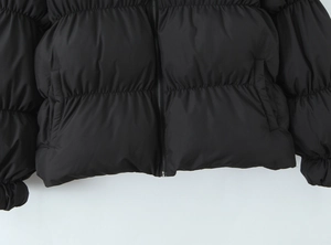Detail view of black puffer jacket showing zipper, side pocket, and horizontal quilting