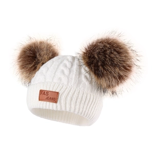 Detailed knit texture of white baby winter hat with double brown faux fur pom poms