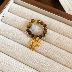 Close-up of tiger eye stone beads with a golden horse charm and ancient coins on a ring