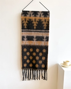 Detail view of mustard yellow and brown knit wall hanging with tassels and geometric patterns