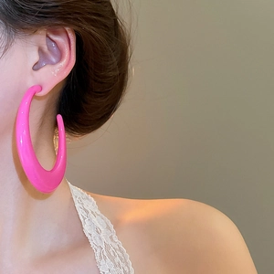 Close-up of hot pink C-shaped earrings with a high-gloss finish worn by a model