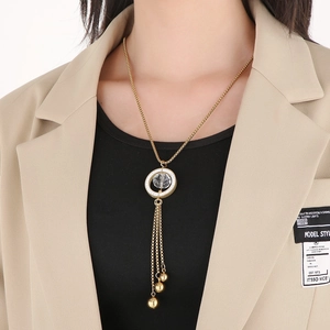 Detail of a gold long necklace with a clear circular pendant and metal ball tassel on a model