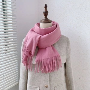 Detailed close-up of soft pink knitted scarf with fringe, worn on a beige wool coat