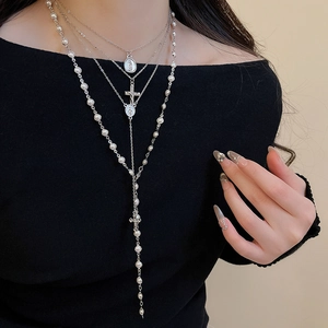 Detailed layered Y2K cross and pearl necklace set shown on a chic black outfit