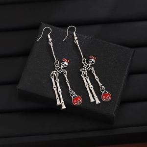 Close-up of skeleton and pumpkin drop earrings on a textured black jewelry box