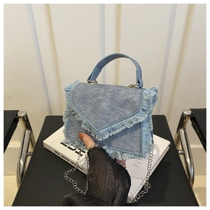 Detail of light blue denim crossbody bag with fringe trim and silver chain strap
