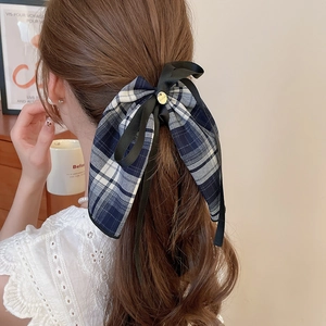 Detail of a navy blue plaid bow hair tie with metal charm on a model's hairstyle