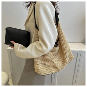 Detail of hand-woven straw tote bag and black PU leather clutch shown with a beige blazer