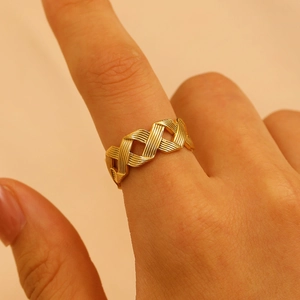 Detailed close-up of a golden braided texture ring worn on a finger against beige backdrop