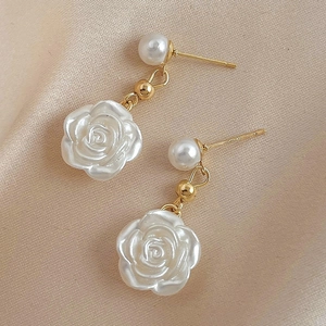 Macro shot of camellia flower drop earrings with pearls on champagne satin fabric