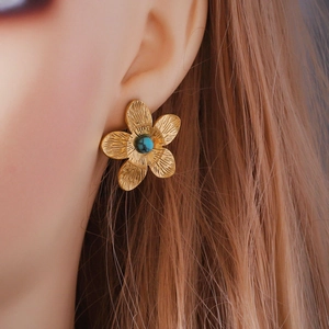 Macro shot of 18K gold plated flower earring with turquoise center on model's ear