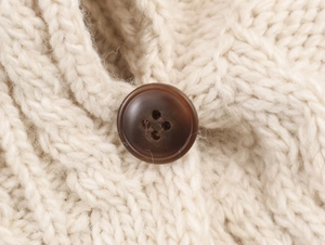 Detailaufnahme von Zopfmuster-Strick und braunem Knopf an einer cremefarbenen Strickjacke