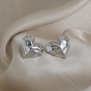 Close-up of heart-shaped silver earrings with geometric diamond-cut texture on silk