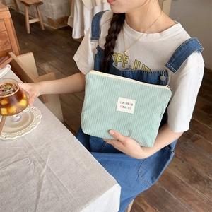 Detailed view of light green corduroy makeup bag with zipper held in a lifestyle setting
