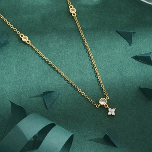 Elegant gold clover necklace with white zircon petals on a dark green background