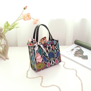 Detail of colorful snakeskin handbag with metal chain strap and silk scarf accessory
