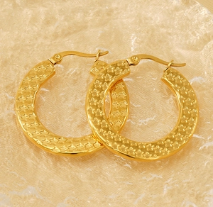 Close-up of golden hoop earrings featuring intricate embossed star texture and a sleek clasp