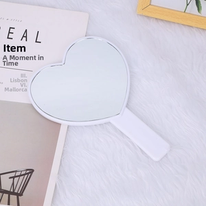 Close-up of heart-shaped handheld mirror with white frame on soft plush background