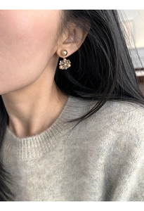 Close-up of golden spherical stud earrings with pearl flower pendant on a model's ear