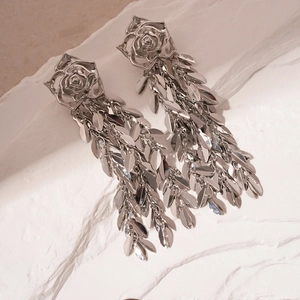 Detailed view of silver rose earrings with leaf tassels on textured stone background