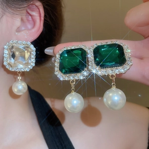 Close-up of vintage emerald and crystal stud earrings with large white pearl pendants