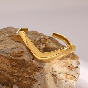Polished wave-shaped 18k gold stainless steel open bangle displayed on a natural rock