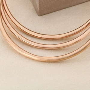 Macro detail of polished 18K rose gold plated round bangles on a beige textured fabric