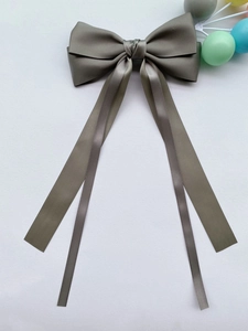 Dettaglio di un grande fiocco per capelli in raso grigio scuro con lunghi nastri fluenti