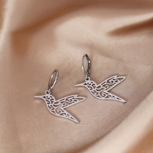 Detailed close-up of hummingbird earrings with silver filigree on champagne satin