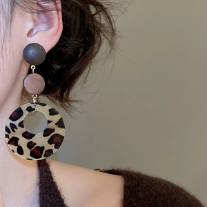 Detailed view of leopard print resin and wood earrings worn by a model in brown knitwear