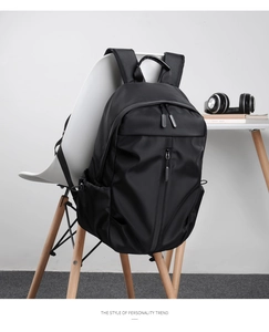 Modern black travel backpack displayed on a white chair in a minimalist home office setting.