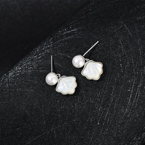 Close-up of elegant shell-shaped silver earrings with pearl accents on black background