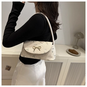 Détail de la broderie florale et du nœud doré sur un sac bandoulière beige tissé