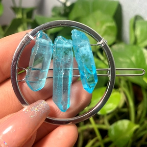 Detailed close-up of a silver circular hairpin featuring three blue crystal stones
