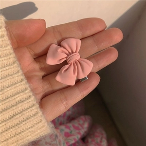 Pink matte bow hair clip with metal duckbill base held on fingertips for size detail
