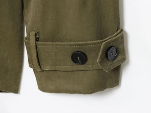 Détail macro des poignets du trench-coat vert olive avec sangles et boutons réglables
