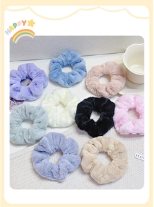 Flat lay of colorful plush scrunchies in various pastel shades on white fabric background