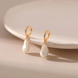 Close-up of gold hoop earrings with natural baroque pearls on a beige ceramic tray