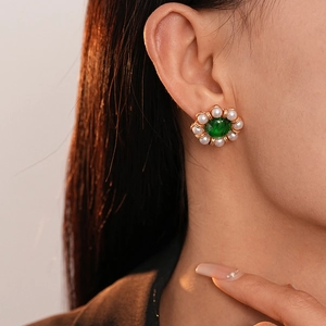 Close-up of vintage flower earrings featuring green stones and pearls on model