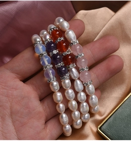 Detailed view of elastic pearl and agate beaded bracelets held in hand with silk background