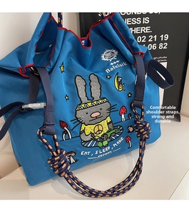 Close-up of blue canvas tote bag featuring cartoon rabbit embroidery and woven rope handle