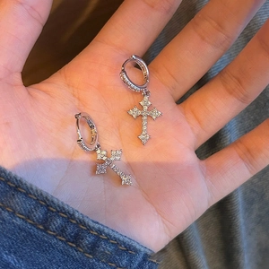 Macro detail of silver cross earrings with sparkling zircon held in palm