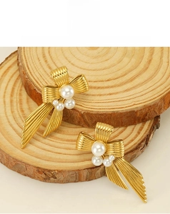 Macro detail of golden bow earrings with pearls on textured wood surface backgrounds
