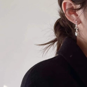Detail of silver drop earrings with layered bell charms and white pearl on model