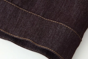 Détail du tissu denim foncé avec des surpiqûres jaune doré contrastées sur l'ourlet