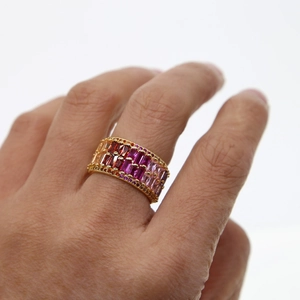 Polished gold ring with pink red and orange gradient zircons on a white background